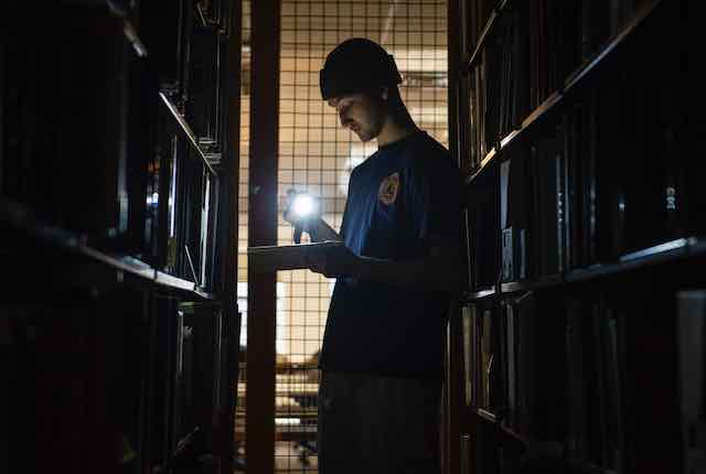 A man with a headlamp in darkened book stacks