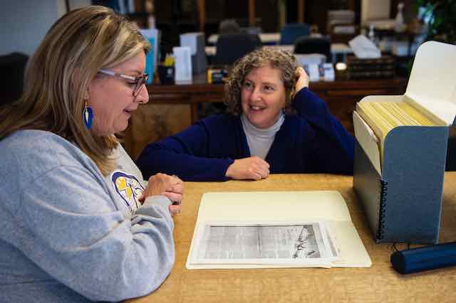 Two women discussing an archival document with an open box on the table.