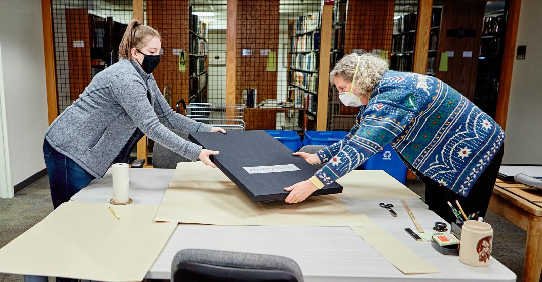 Photo of two library staff members packaging a collection before putting it away.